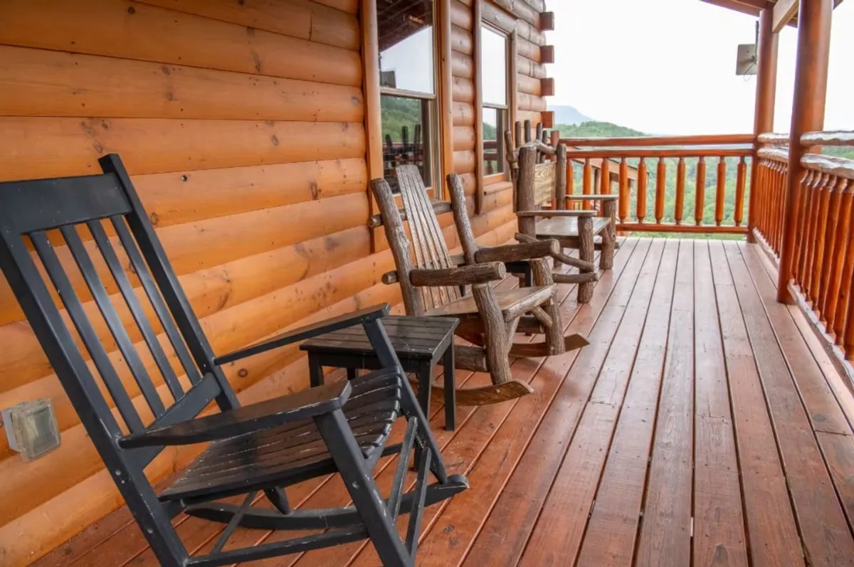 A cozy cabin porch with wooden rocking chairs facing outward, overlooking the serene natural setting. The logs and wooden railings emphasize rustic elegance, while the inviting chairs suggest relaxation and intimate conversations at sunset.