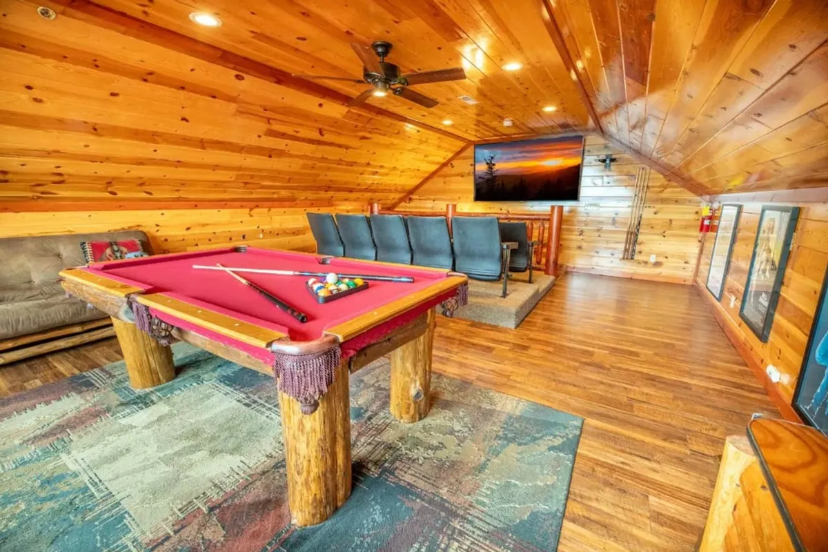 A vibrant game and media room is centered around a pool table, surrounded by a comfortable seating area and a large television. The wooden walls lend warmth, while the arrangement encourages both competitive play and group relaxation.