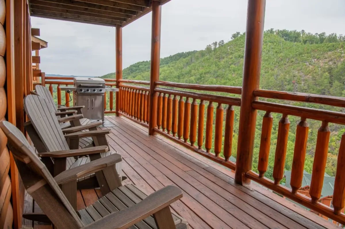 A balcony with wooden chairs and a BBQ grill sits high above the mountain landscape. The seating area provides a perfect vantage point for sunrise breakfasts, sunset dinners, or simply soaking up the serene surroundings.