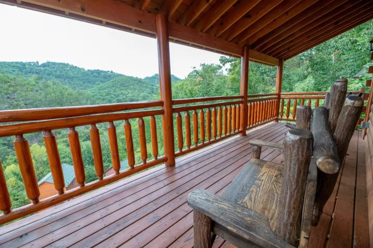A serene view from a wooden deck with rocking chairs facing a sweeping mountain vista. The tranquil setting is perfect for unwinding, socializing, and soaking in natural beauty after a day of exploration or celebration.