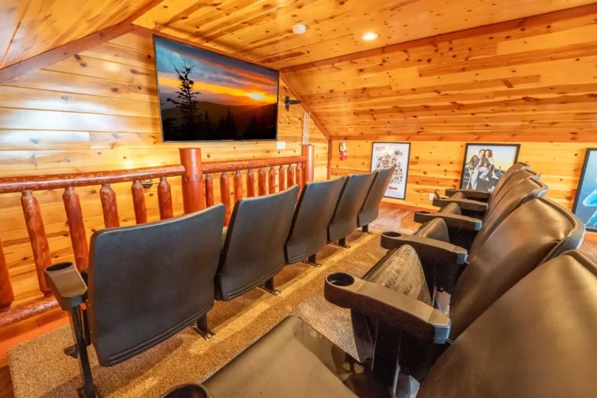 The scene presents a dedicated theater area with plush theater seating facing a large flat screen TV. Wooden wall paneling and decorative posters create an authentic cinema-inspired atmosphere, perfect for immersive movie nights or catching sports events.
