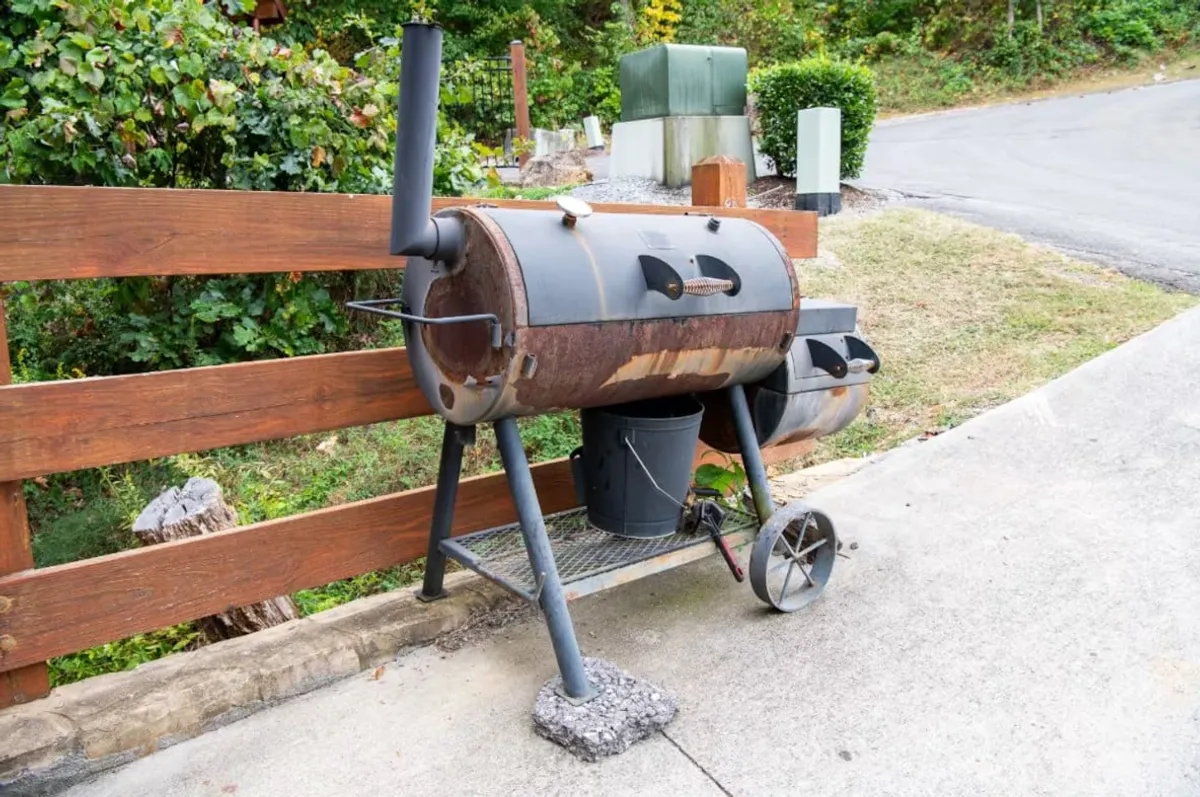 An inviting outdoor area with a smoker grill, wooden fence, and surrounding greenery. The setup is designed for barbecues, outdoor cooking, and memorable gatherings with friends and family.